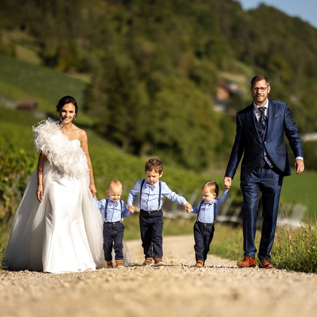 Eine Familie – ein Paar und drei Jungen – spaziert durch einen Weinberg mit grünen Hügeln im Hintergrund.